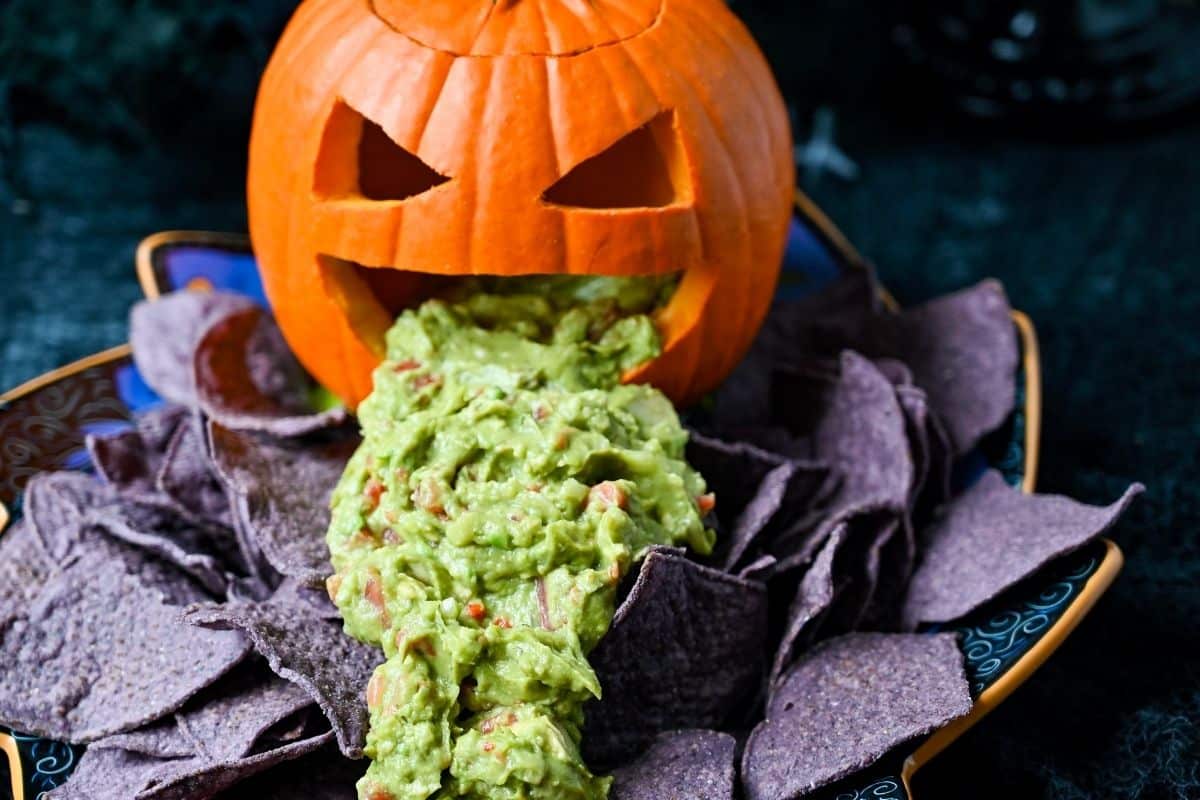 blue corn chips surrounding a guacamole puking pumpkin on a halloween platter