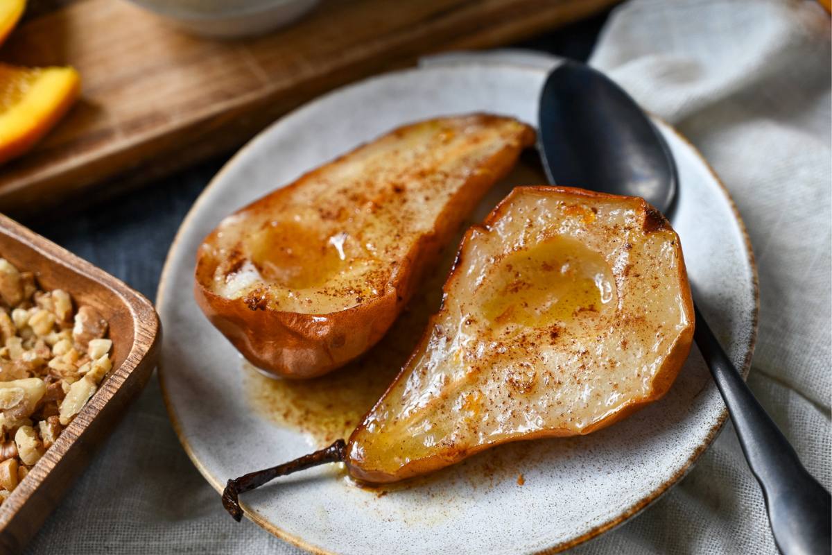 close up of two roasted maple butter pears cooked in an air fryer on a plate with a spoon