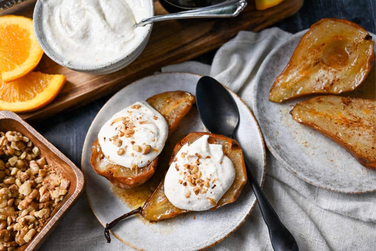 air fryer pear halves with one plate topped with a sweetened whipped cottage cheese and the other plain with a bowl of chopped walnuts for topping