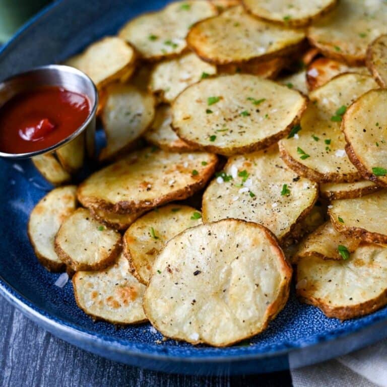 air fryer sliced potatoes garnished with salt and fresh parsley with a side of ketchup