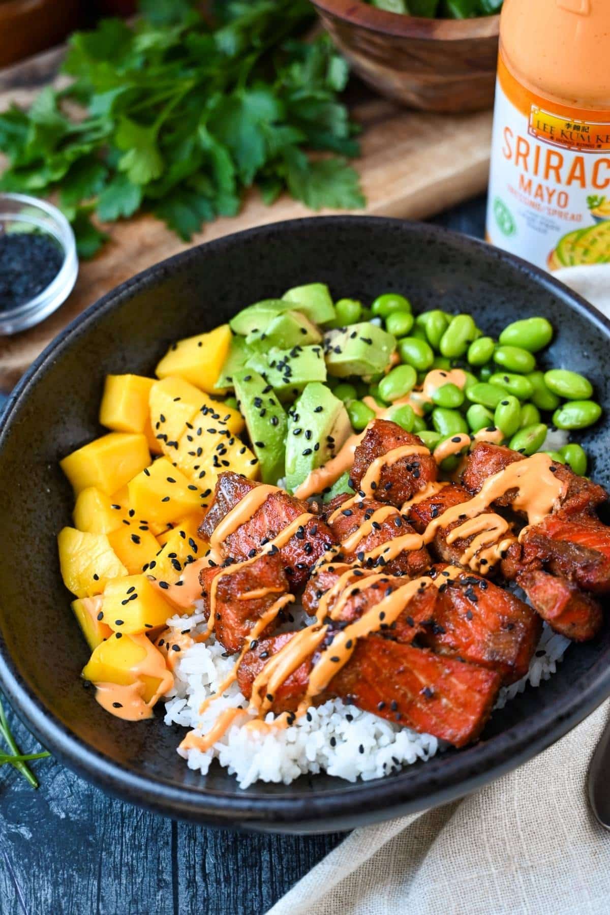 a poke salmon bowl with a bottle of Sriracha mayo behind it