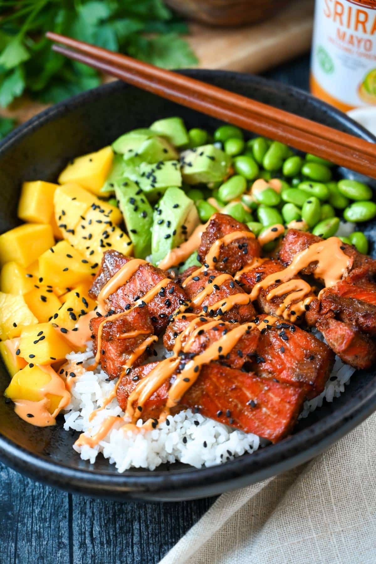 a poke bowl with cooked salmon, edamame, mango, and rice