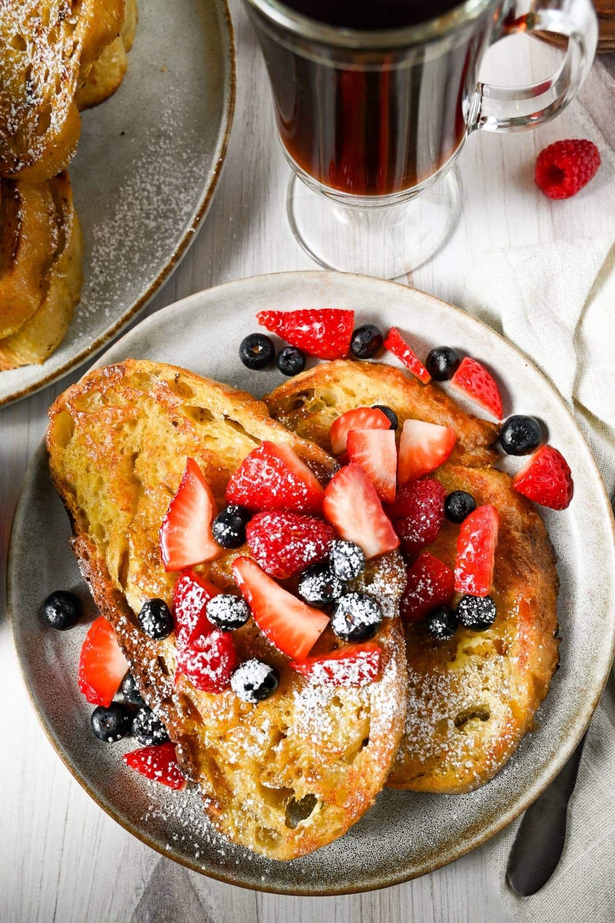 two slices of sourdough french toast on a plate topped with berries and powdered sugar