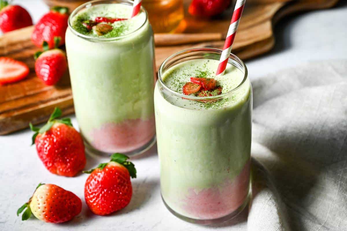 whole strawberries next to two smoothies in glasses with straws