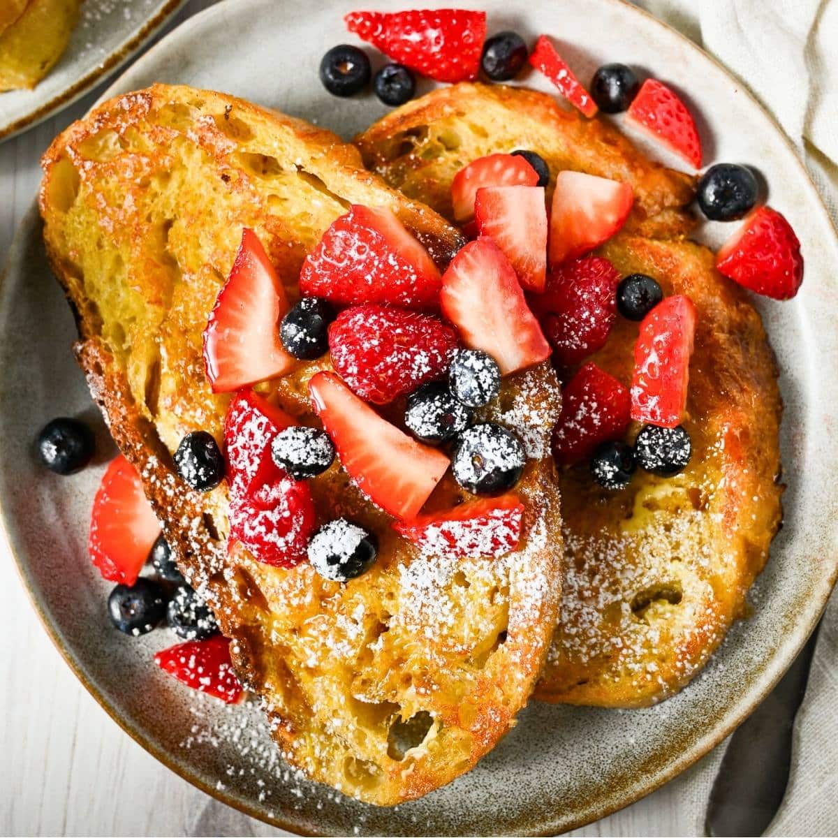 close up of plated sourdough french toast with berries and powdered sugar