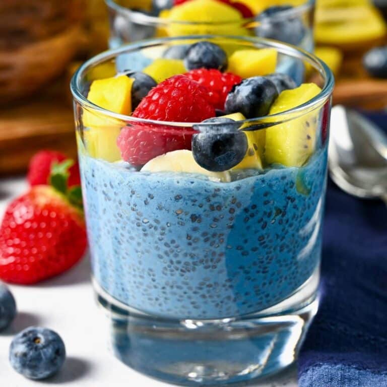 close up of blue chia pudding in a glass with fruit