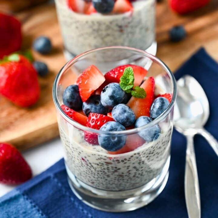 two chia flax puddings in glasses topped with berries with a napkin and spoons