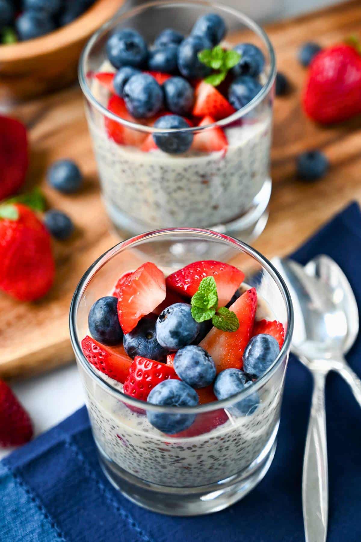 two chia flax puddings with fresh berries on a blue napkin with a cutting board with berries on it