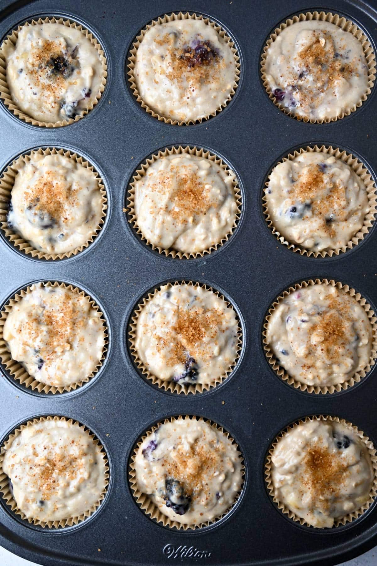 banana muffin batter in muffin tin with turbinado sugar on top