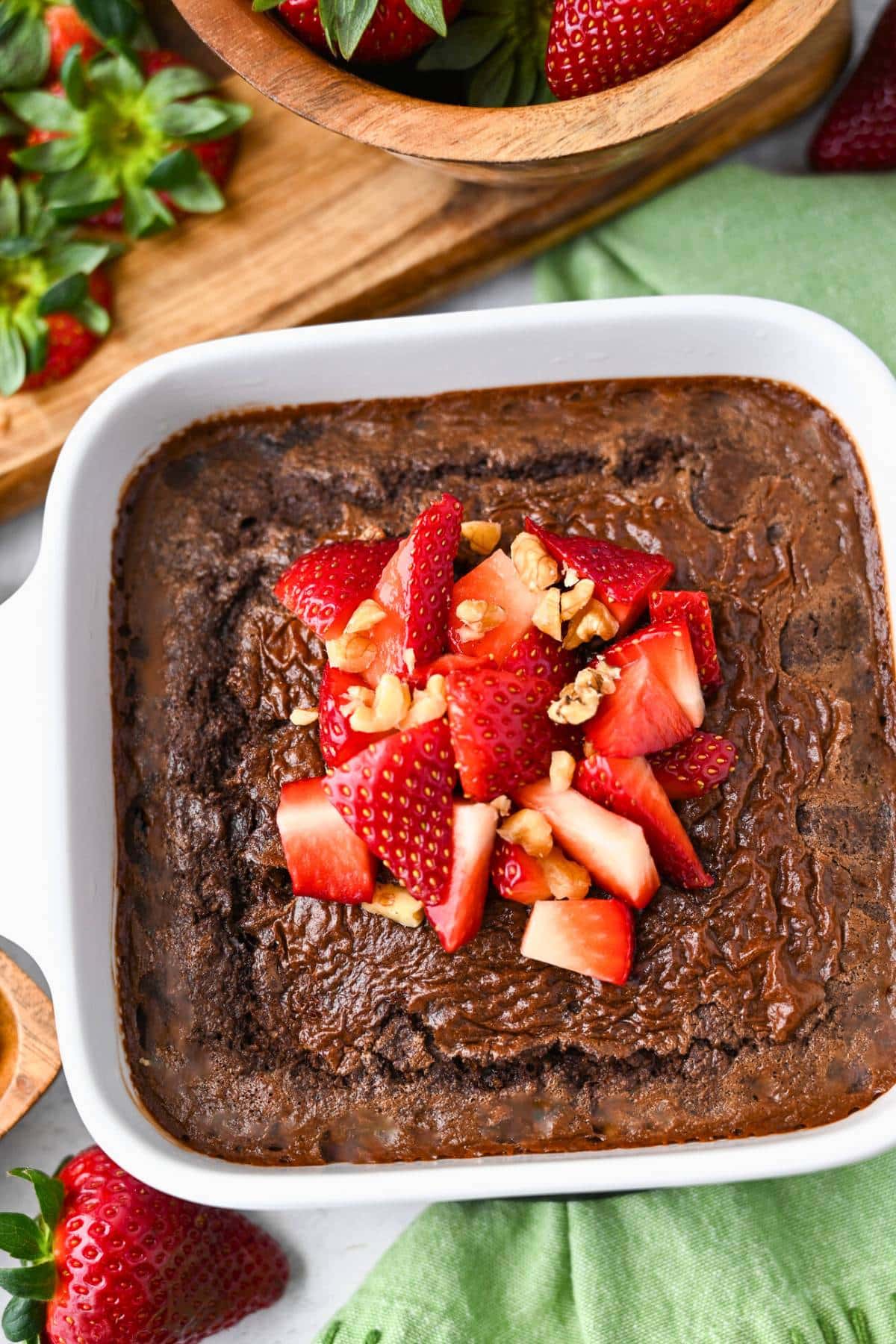 looking down at baked brownie oats in a white dish with strawberries and walnuts on top