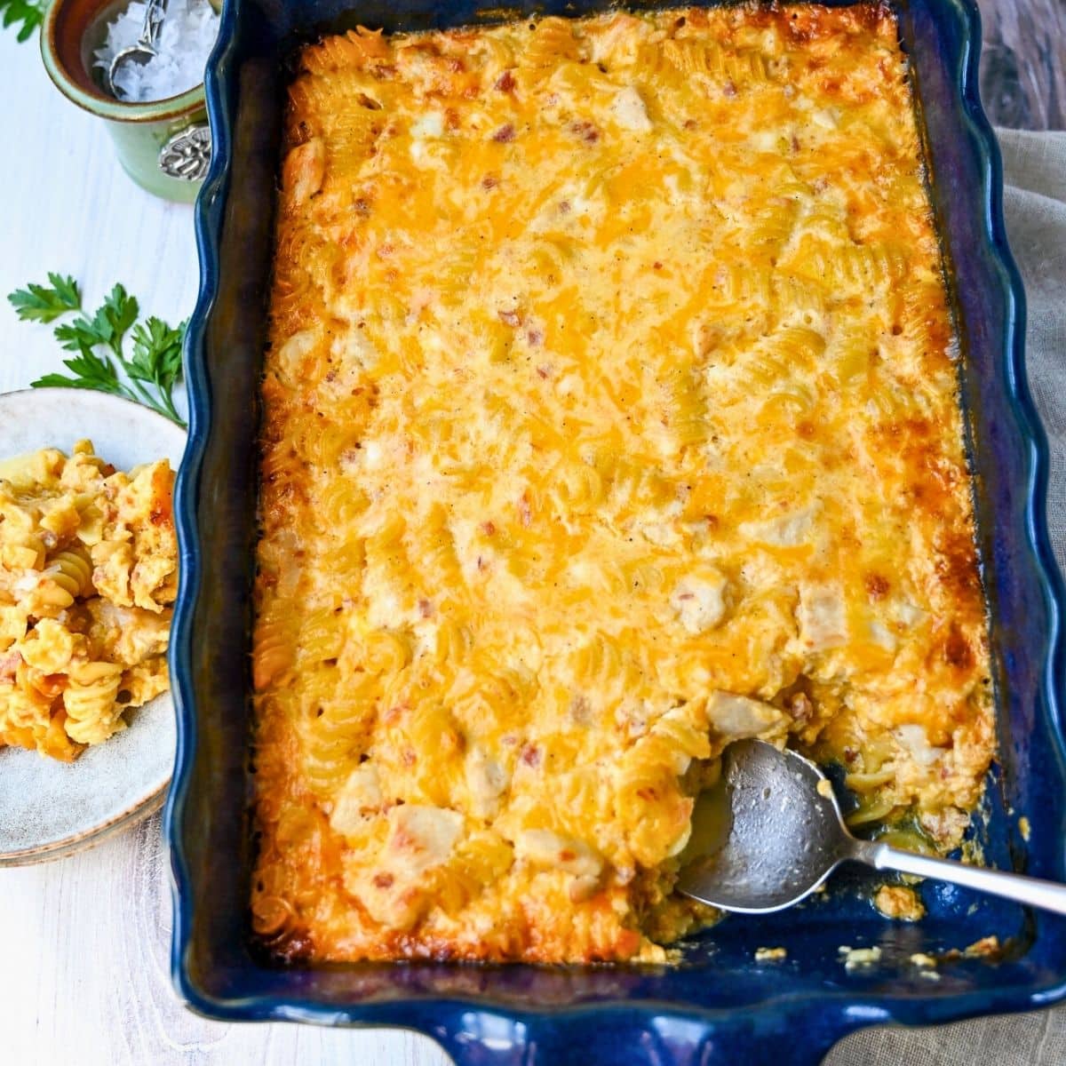a pan of baked mac and cheese with chicken and a served plate with a jar of salt