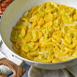 close up of stewed squash in a white deep skillet with bacon and onions