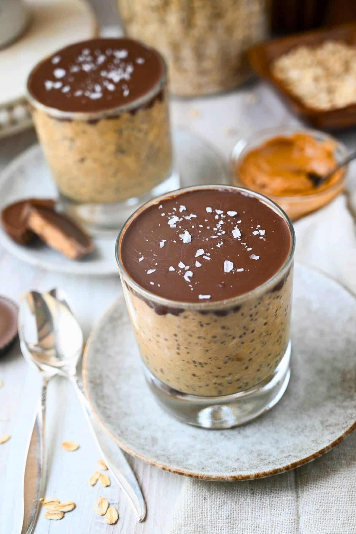 two reeses overnight oats jars with hard magic shell chocolate topping with a jar of oats, sliced peanut butter cups, and a dish of peanut butter