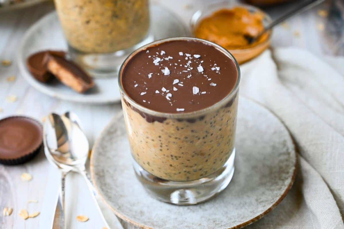 two jars of reeses overnight oats with sliced peanut butter cup and a pb cup in a wrapper with two spoons