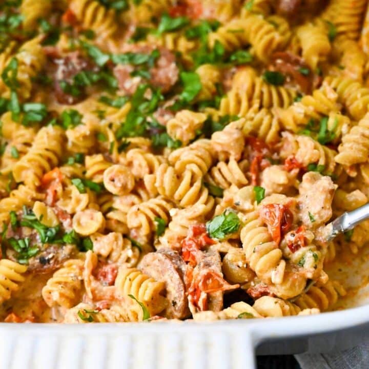 boursin tomato pasta with Italian sausage in a casserole dish with a spoon