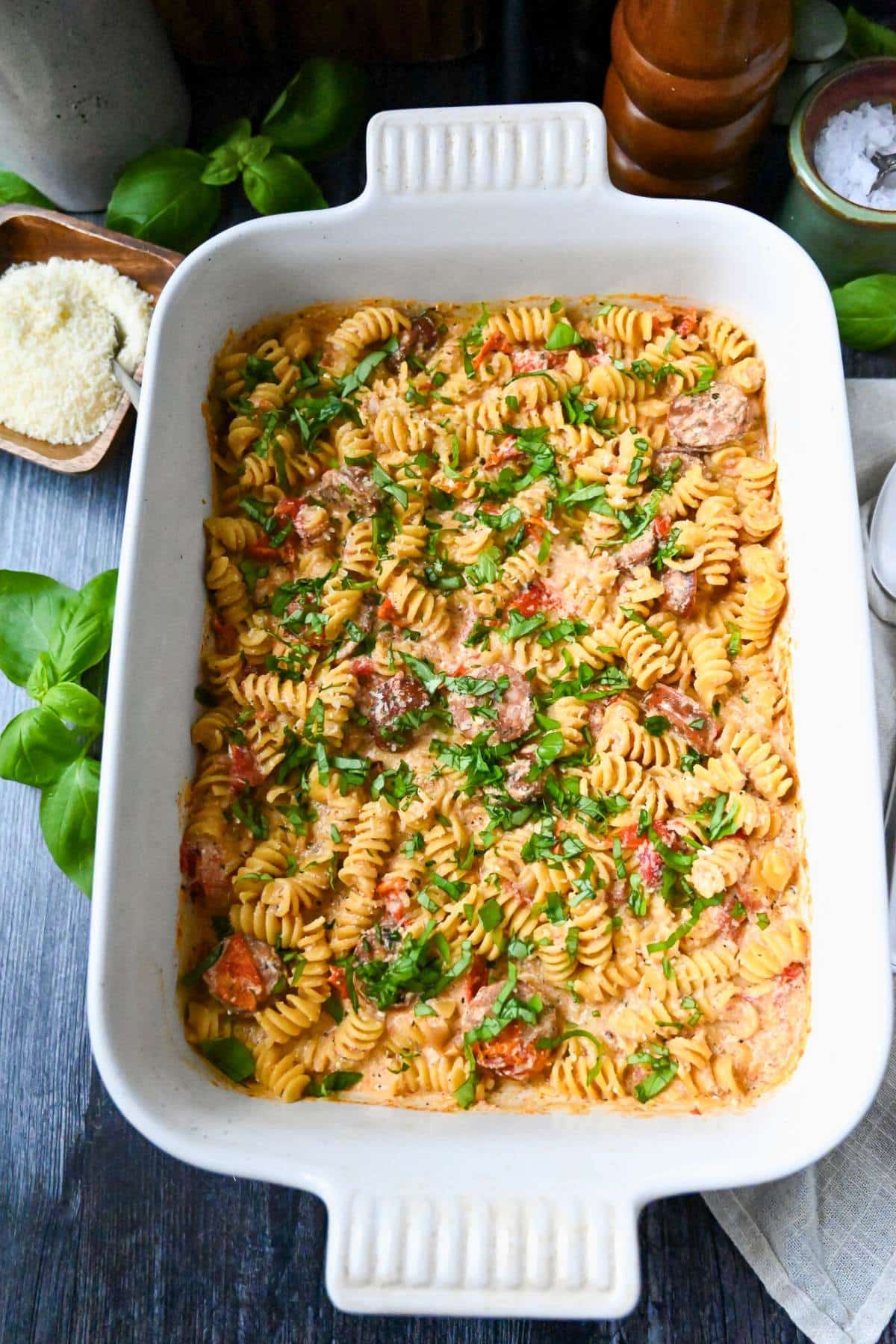 a pan of creamy boursin pasta with tomatoes and Italian sausage with fresh basil and parmesan cheese on the side