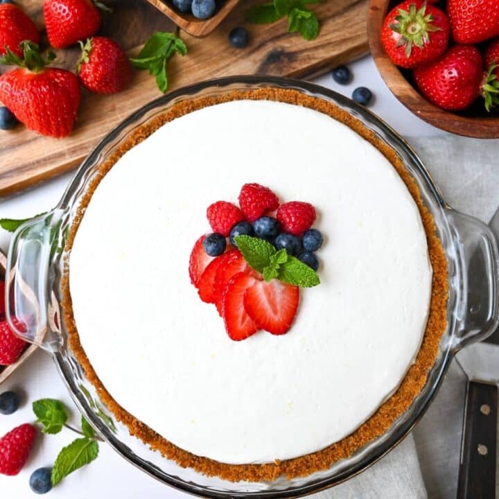 a no bake cheesecake surrounded by berries with strawberries, blueberries, and a mint sprig on top