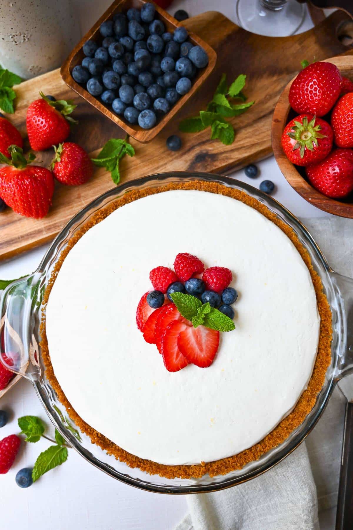 a whole no bake protein cheesecake with berries and mint on top with berries all around it