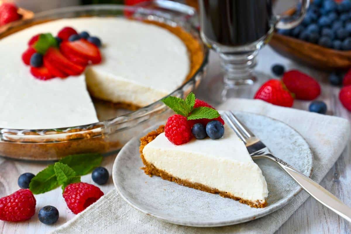 side view of a sliced no bake cheesecake with a slice of cheesecake with berries on a plate with a fork