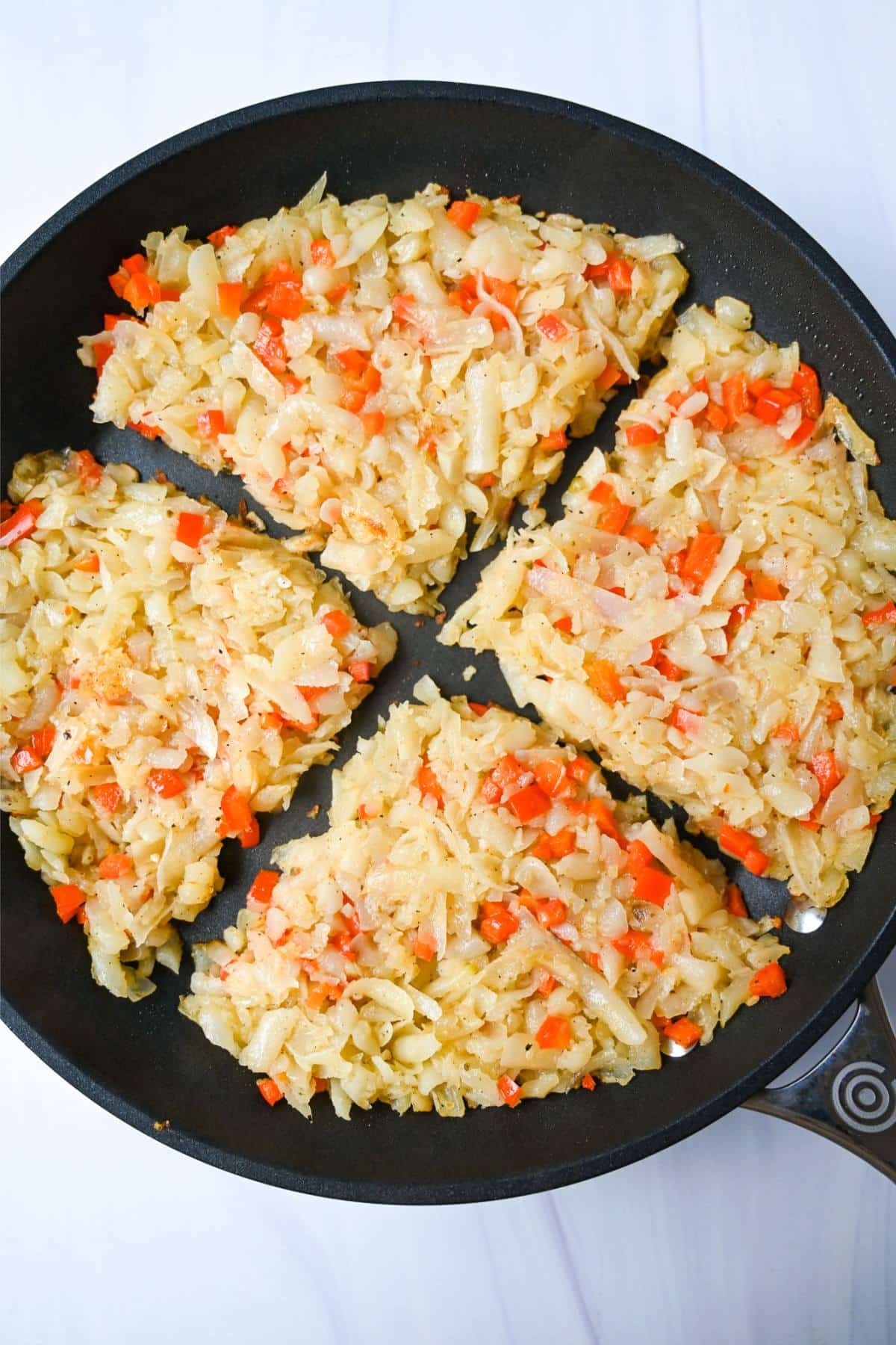 hasbrowns and red pepper divided in four sections in a skillet