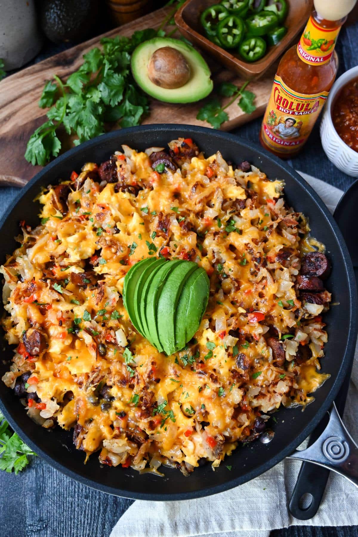 looking down at a breakfast skillet with a sliced half avocado on top with a bottle of hot sauce and half and avocado on the side