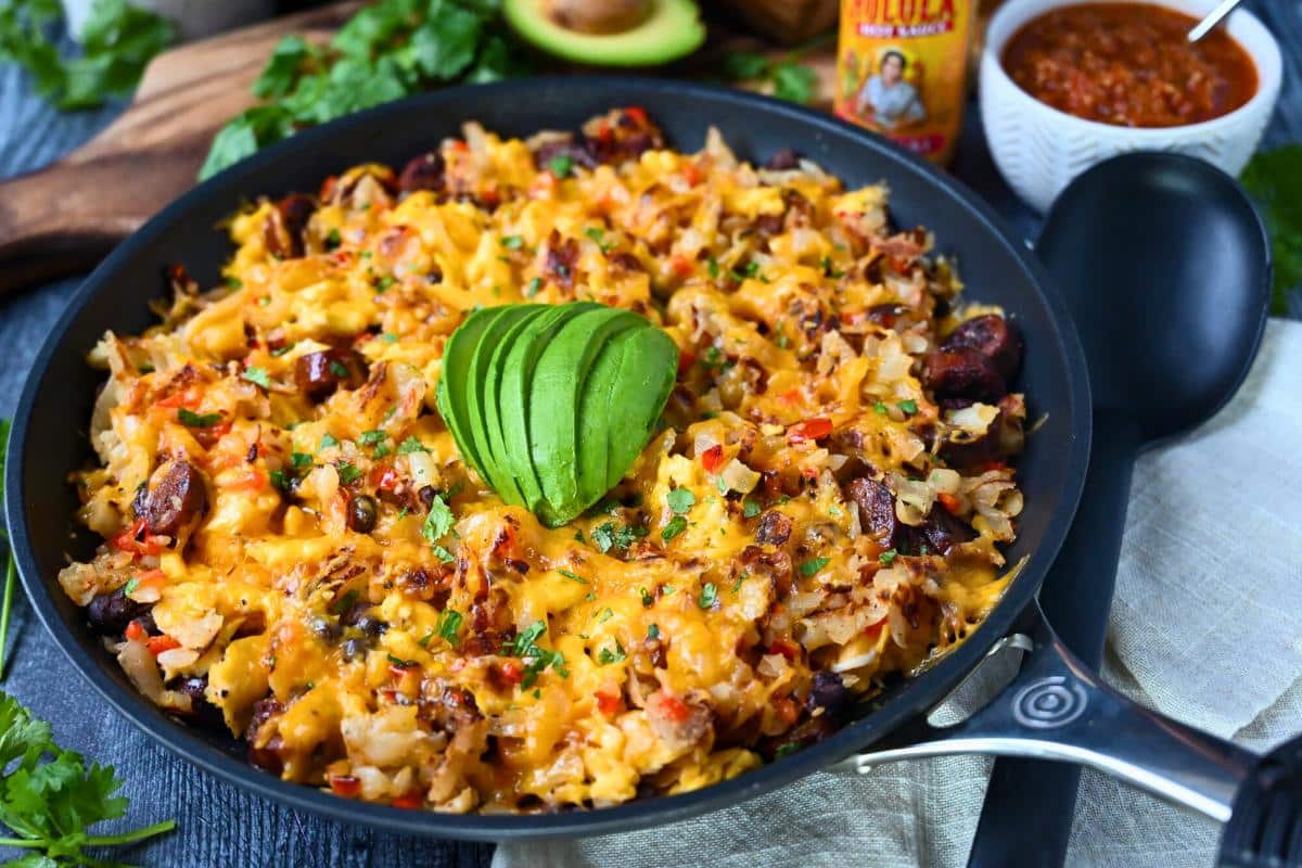 side view of a loaded breakfast skillet with a bowl of salsa and avocado