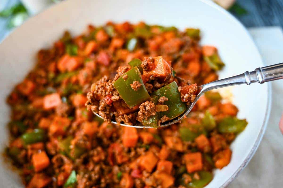 holding up a spoonful of ground beef, sweet potatoes, and peppers sauteed with spices