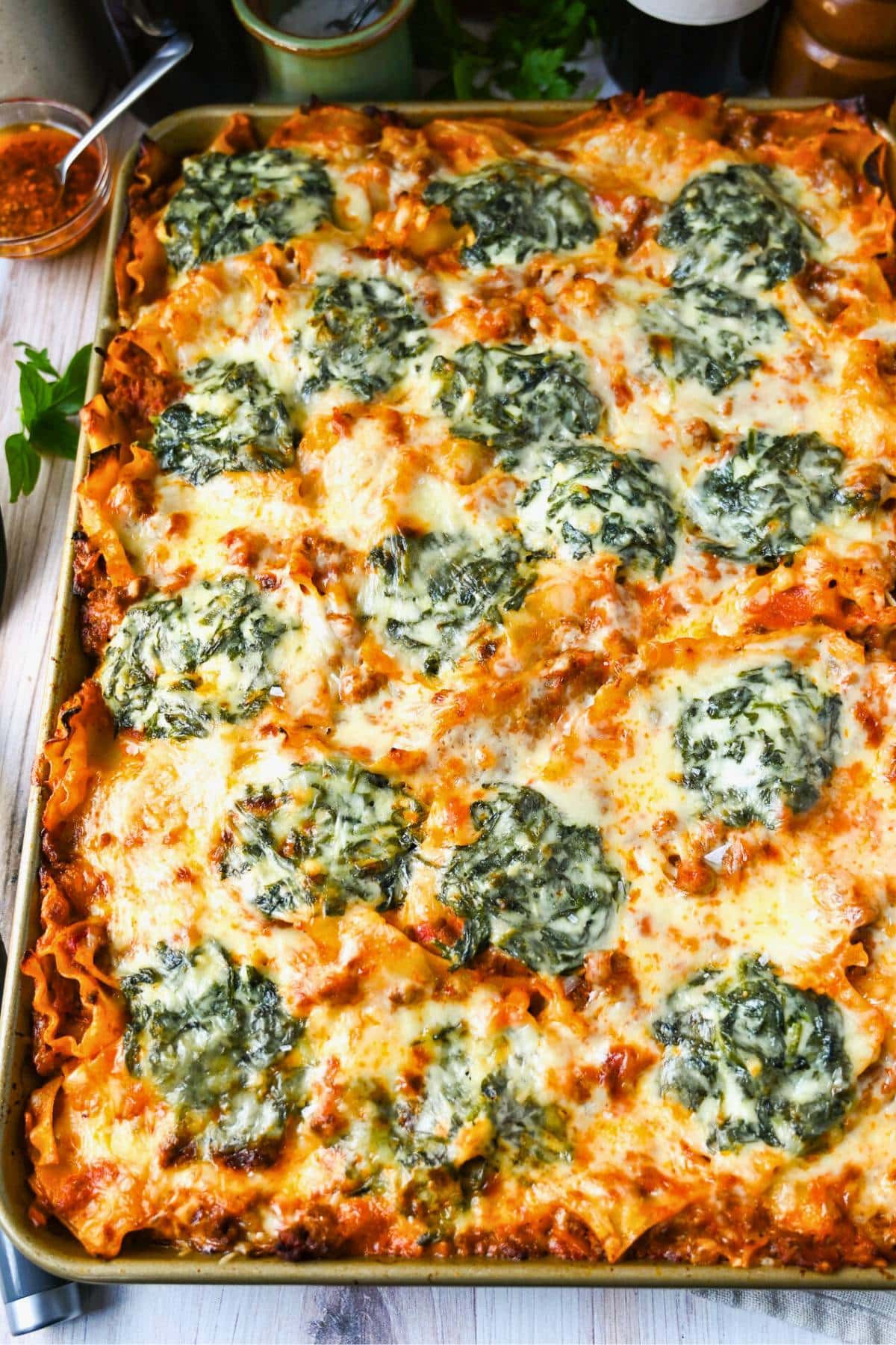 sheet pan lasagna on a table with wine, salt, pepper, and fresh herbs