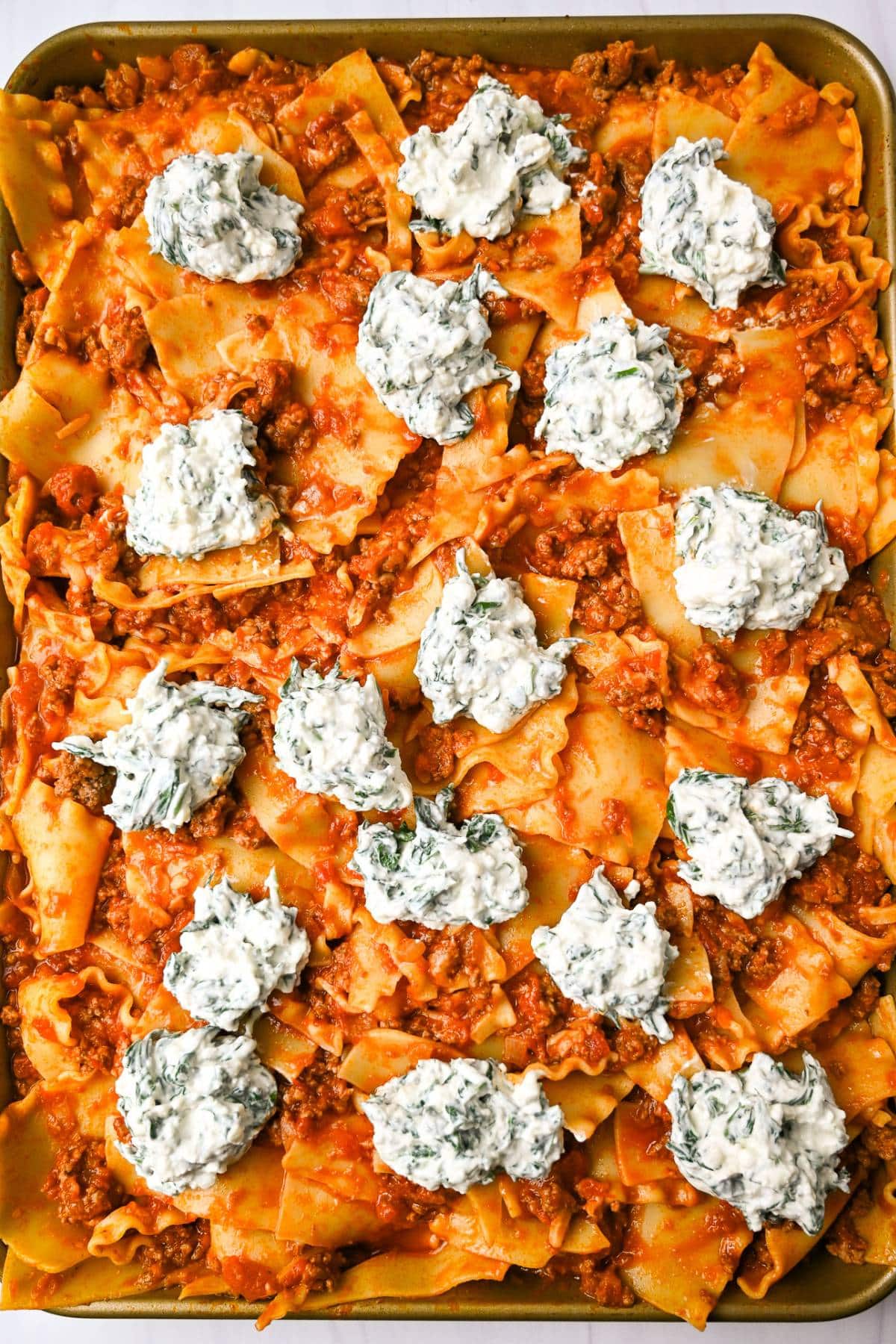 saucy lasagna noodles on a sheet pan topped with dollops of whipped cottage cheese and spinach