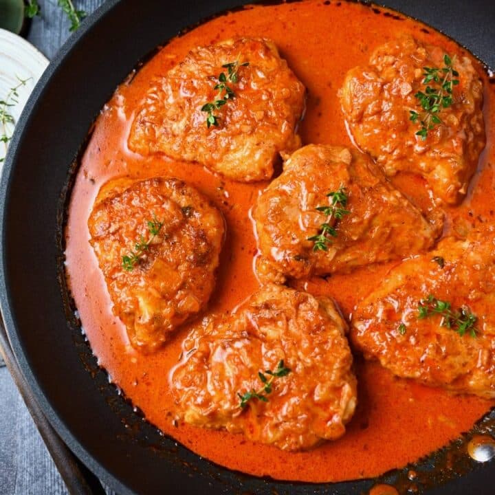 looking down at a skillet of paprika chicken with with a sprig of thyme