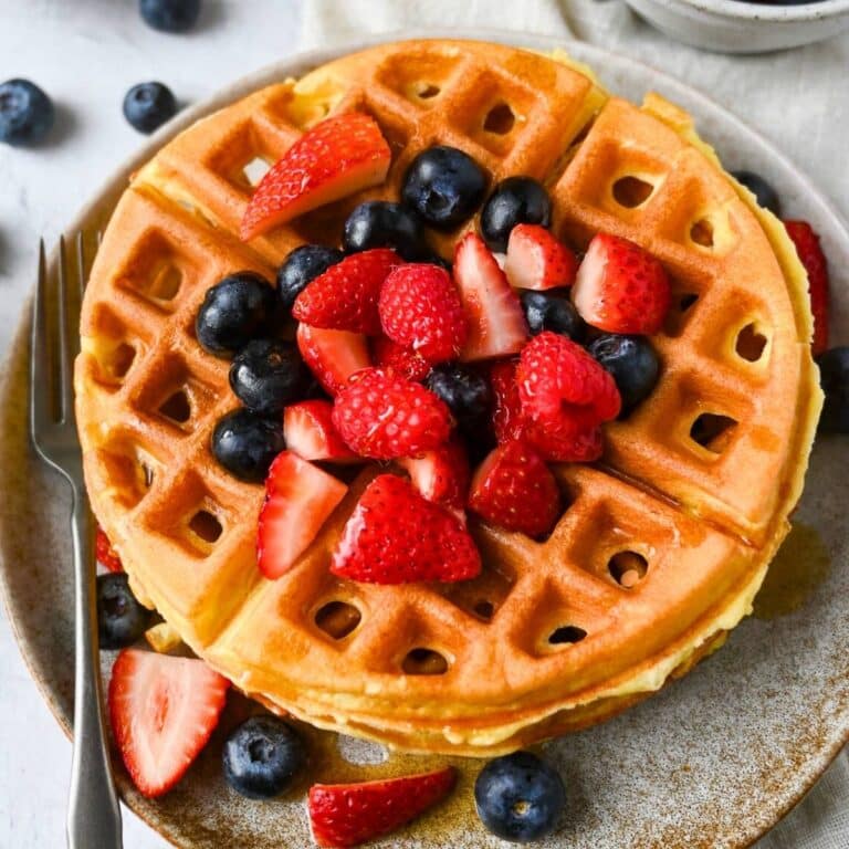 a stack of waffles on a plate with mixed berries and syrup