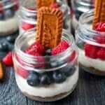 a mini biscoff cheecake topped with raspberries and blueberries with a cookie on the side