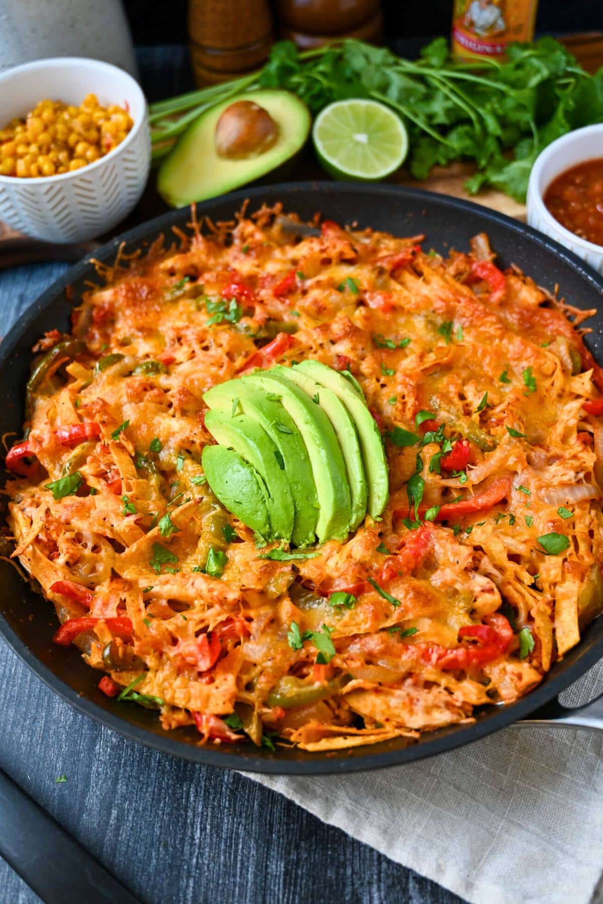 a fajita casserole in a skillet with sliced avocado and toppings in the background