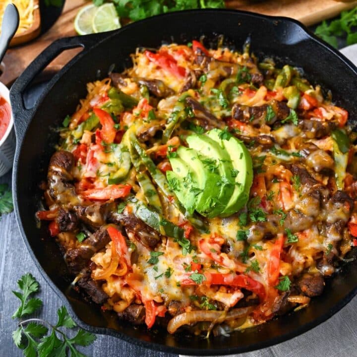 a steak fajita skillet with melted cheese and avocado on top