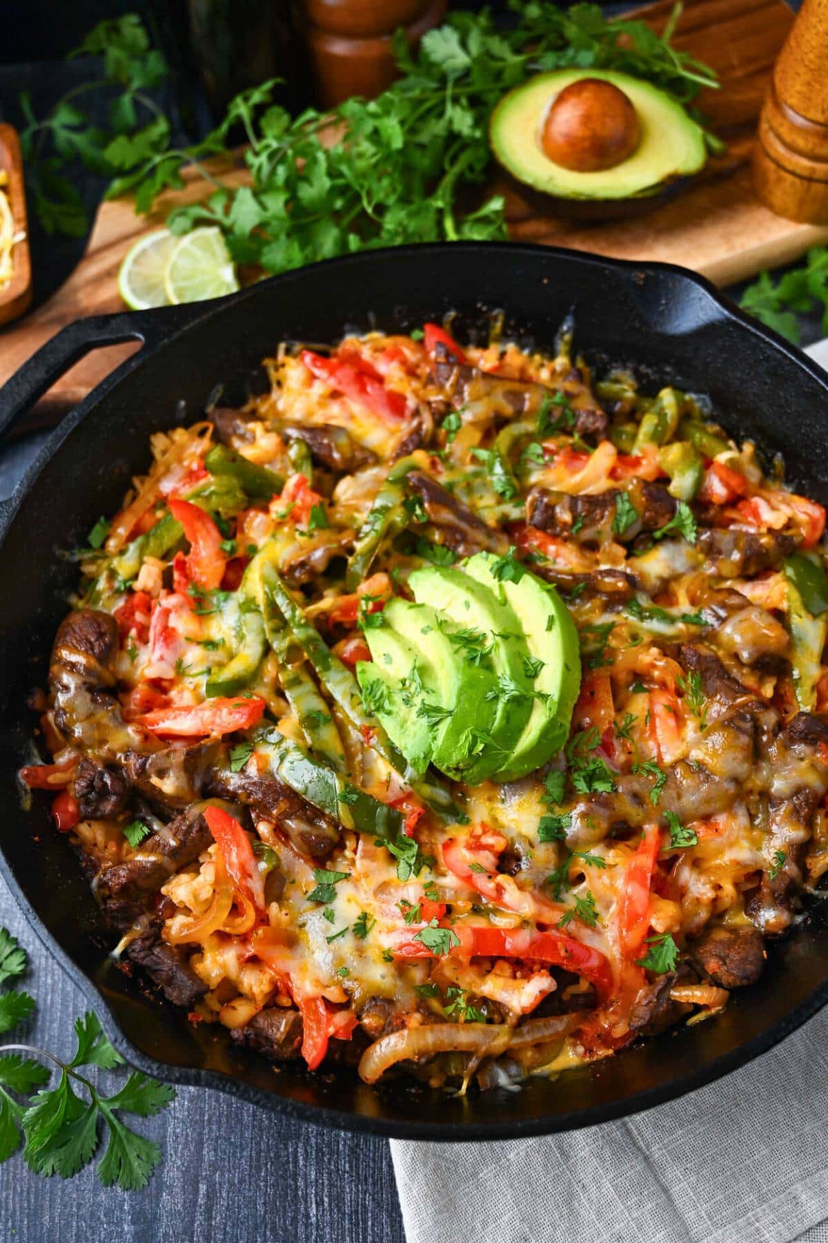 looking down at a steak fajita skillet with rice topped with sliced avocado and cilantro