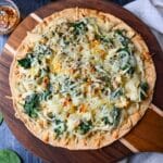 close up of a baked tortilla pizza with chicken, spinach, and artichokes