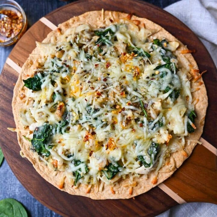 close up of a baked tortilla pizza with chicken, spinach, and artichokes