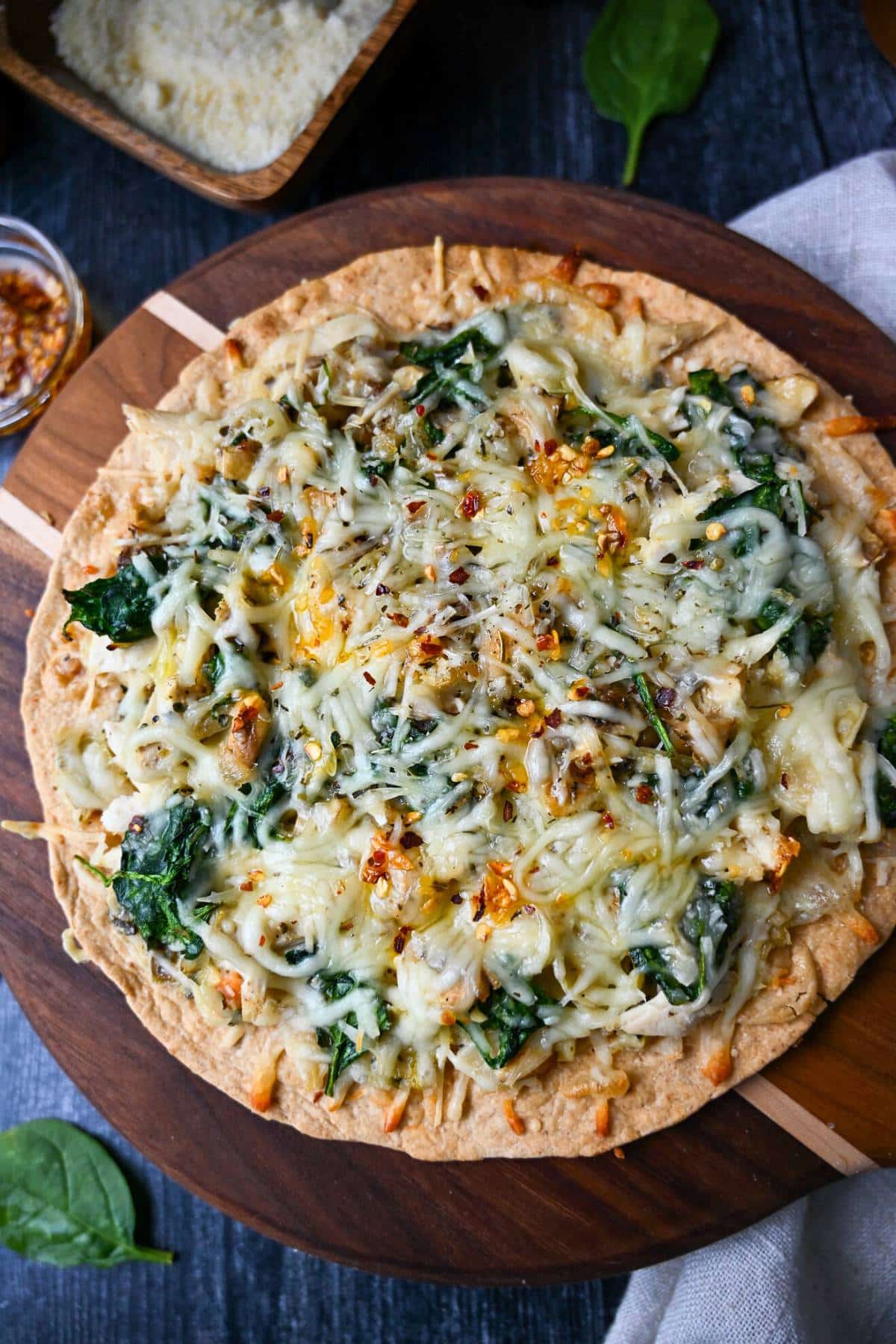 a cutting board with a tortilla pizza on it with a bowl of parmesan cheese next to it