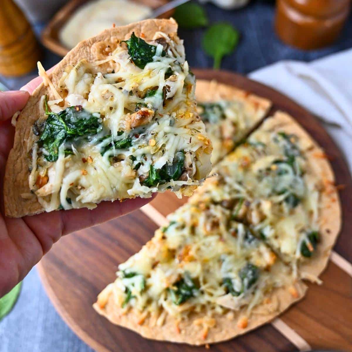 holding up a slice of tortilla pizza