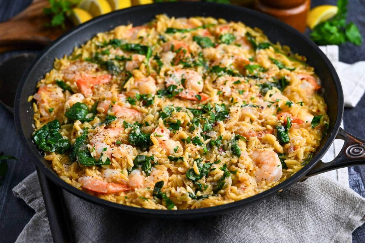 side view of a skillet with shrimp and orzo pasta