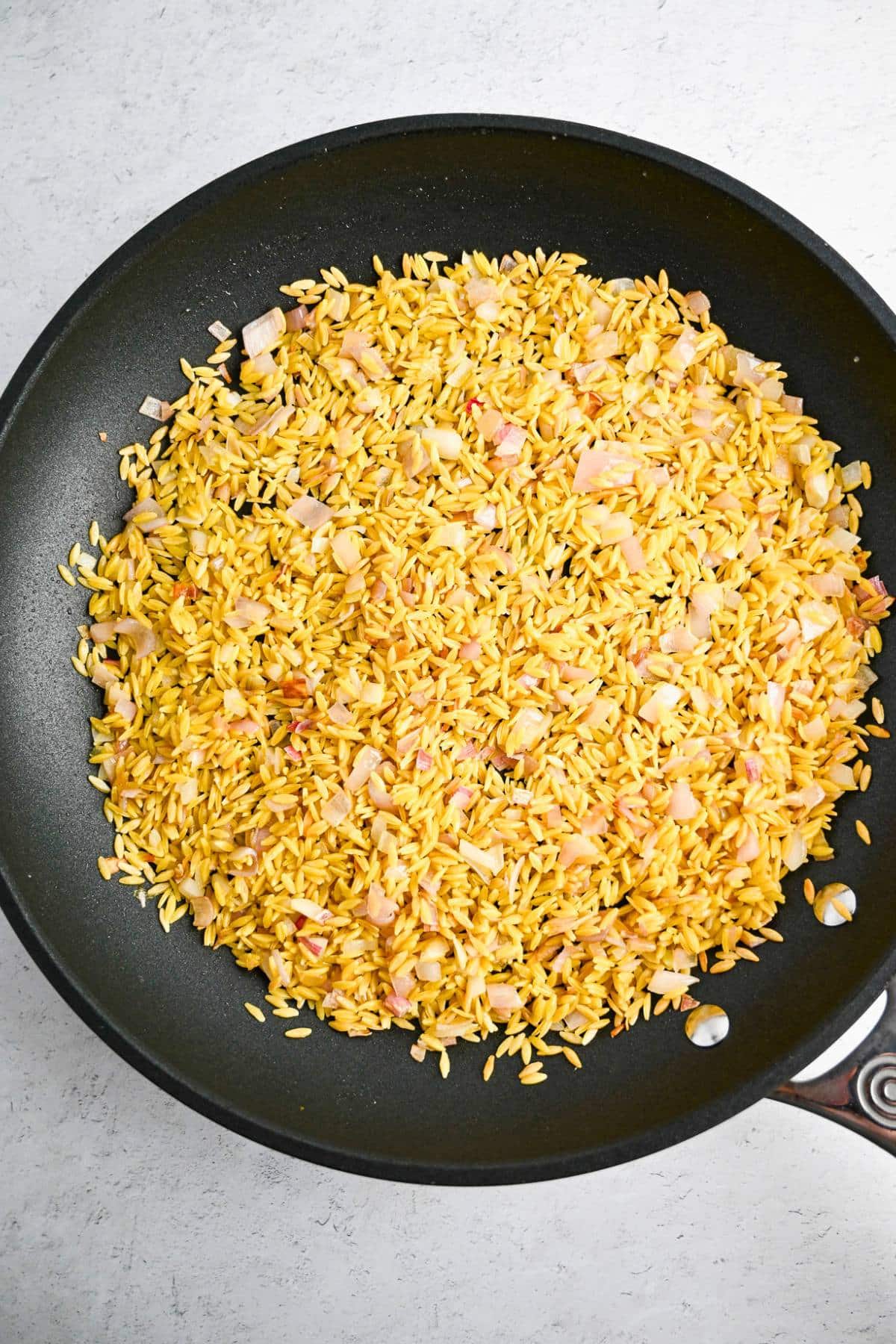 dry orzo and shallots cooked in a skillet