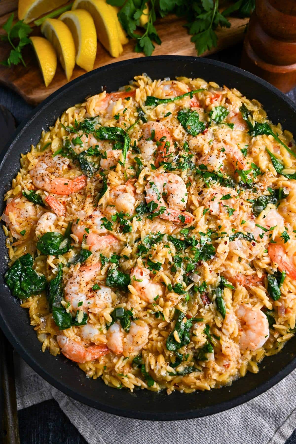 close up of a lemon shrimp orzo skillet with spinach and sliced lemons on a cutting board