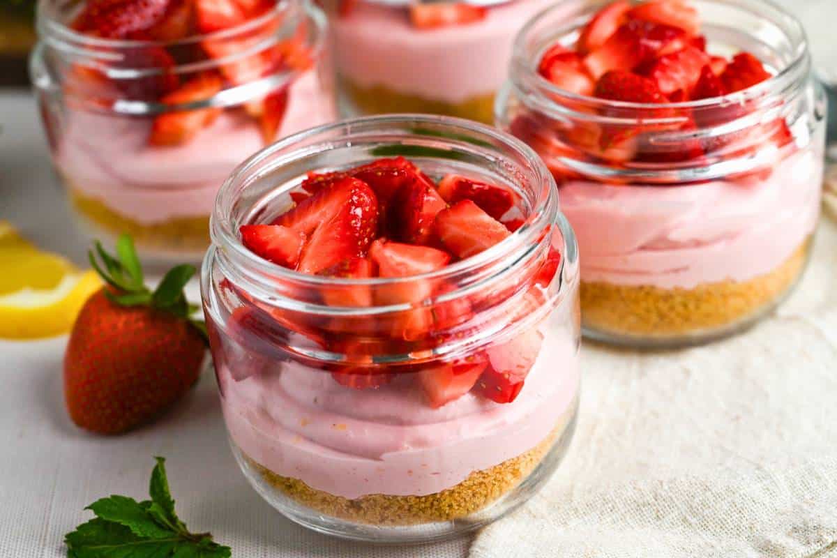 close up of mini strawberry cheesecakes with a graham cracker crust layer and fresh berries on top