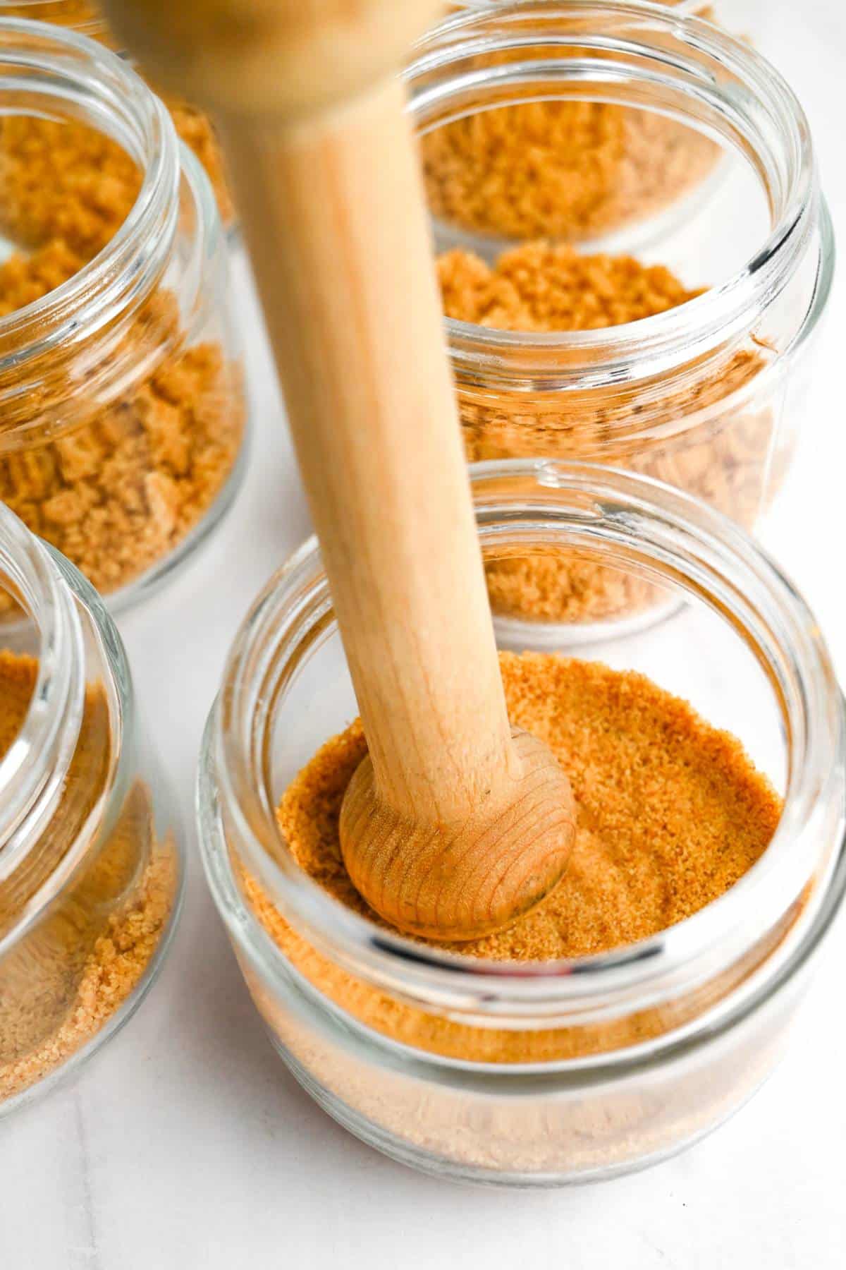 pressing down graham cracker crust in mini jars with a tart tamper