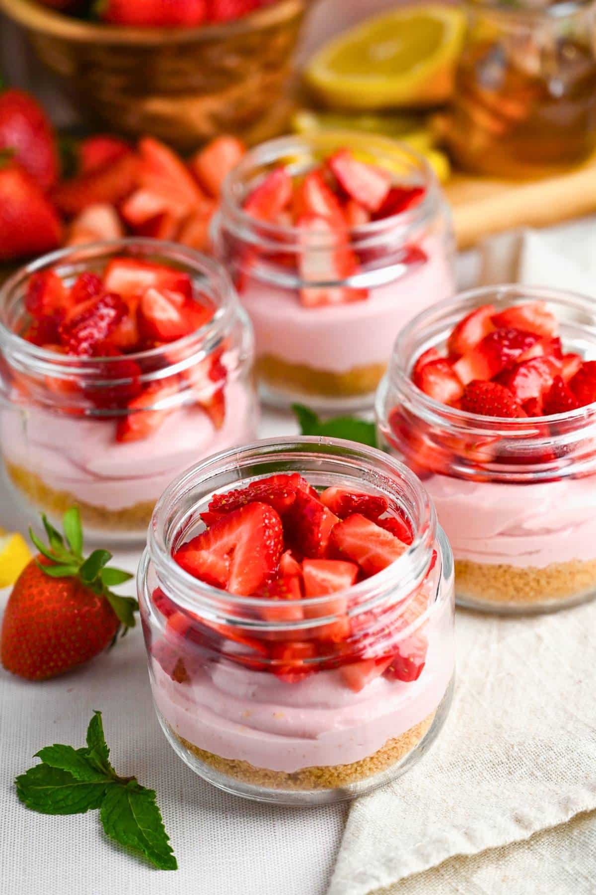 strawberry cheesecake parfaits with a cutting board with lemons, honey, and strawberries behind them