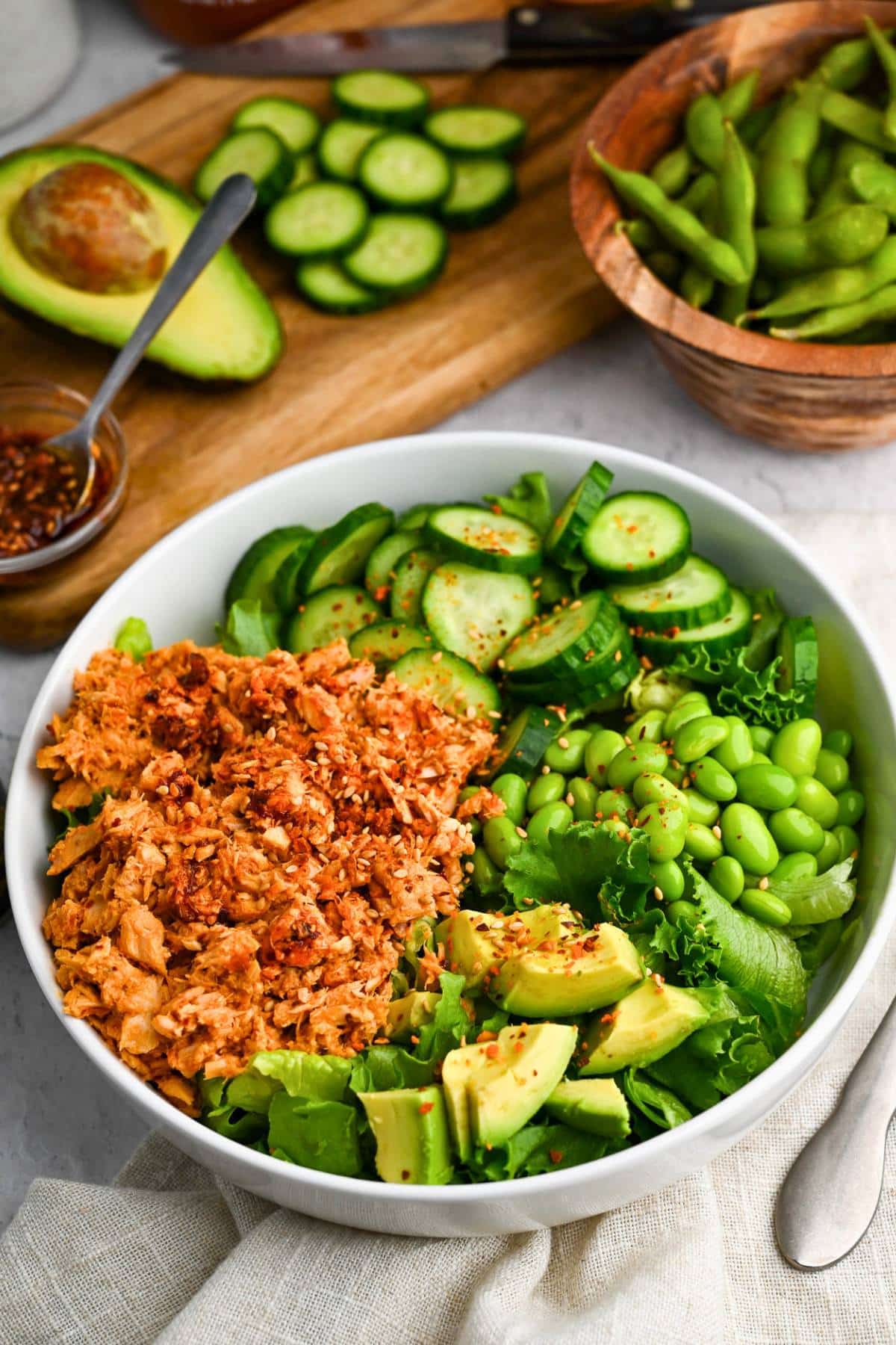 a spicy tuna bowl with a cutting board with cucumbers and avocado