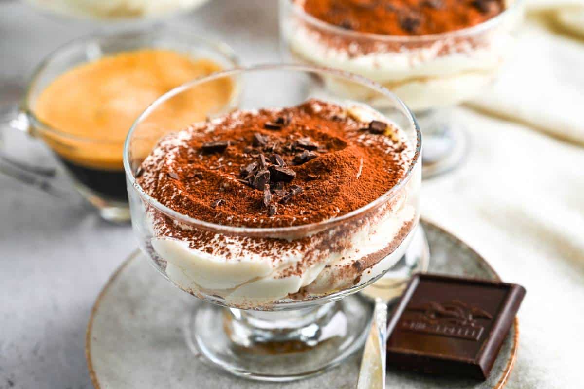 a tiramisu parfait on a plate with a square of chocolate and spoon