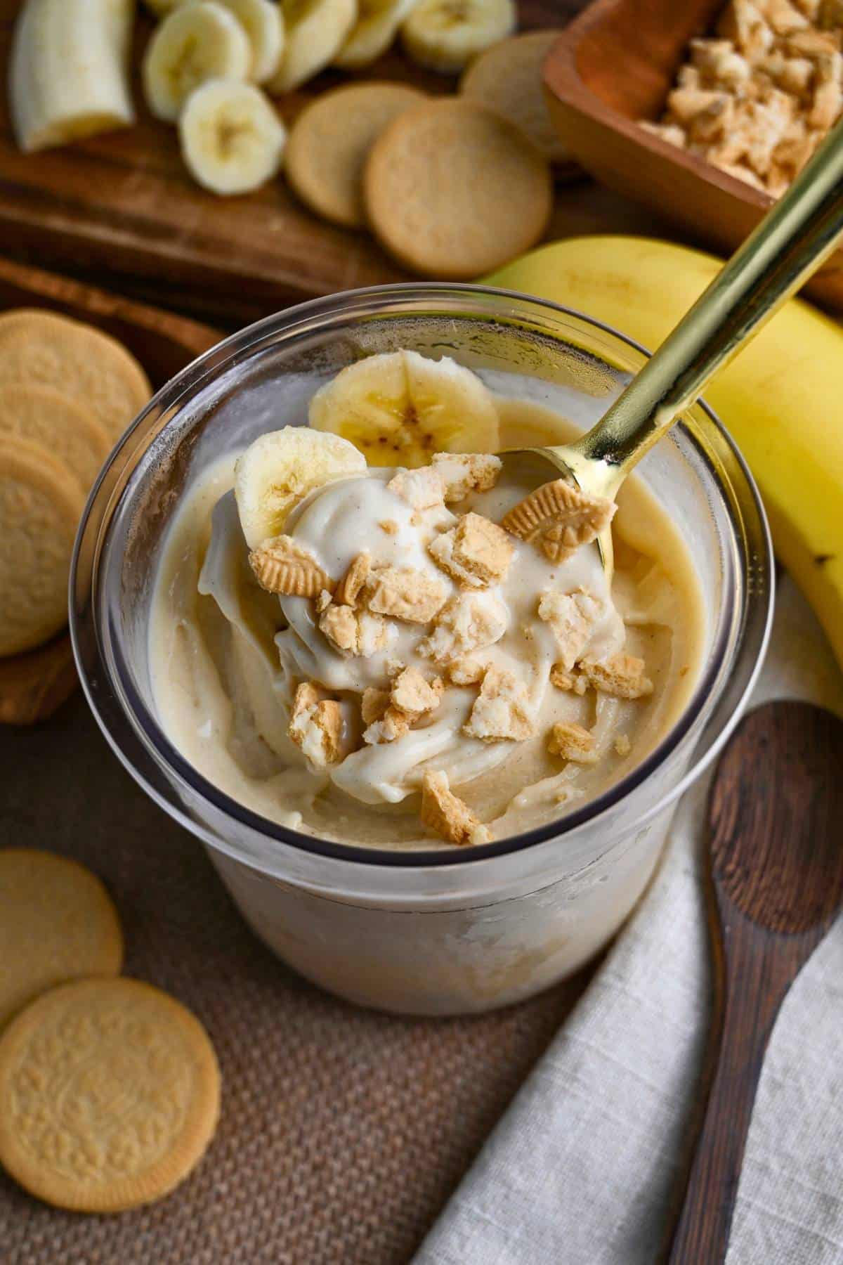 looking down at a container of banana pudding ice cream in a Creami pint with a spoon and crumbled golden oreos and sliced banana on top