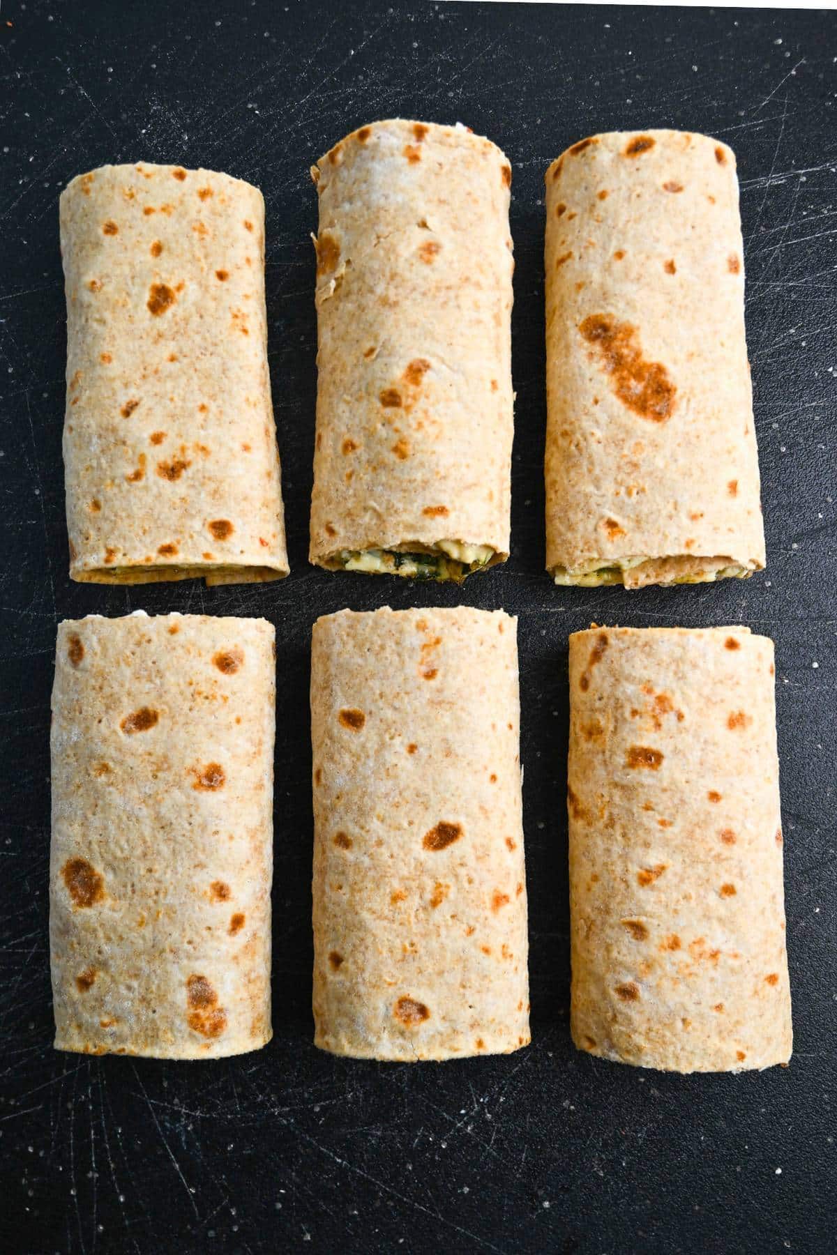 6 lavash breakfast wraps made with egg whites, spinach, sundried tomatoes, and feta cheese rolled up on a cutting board