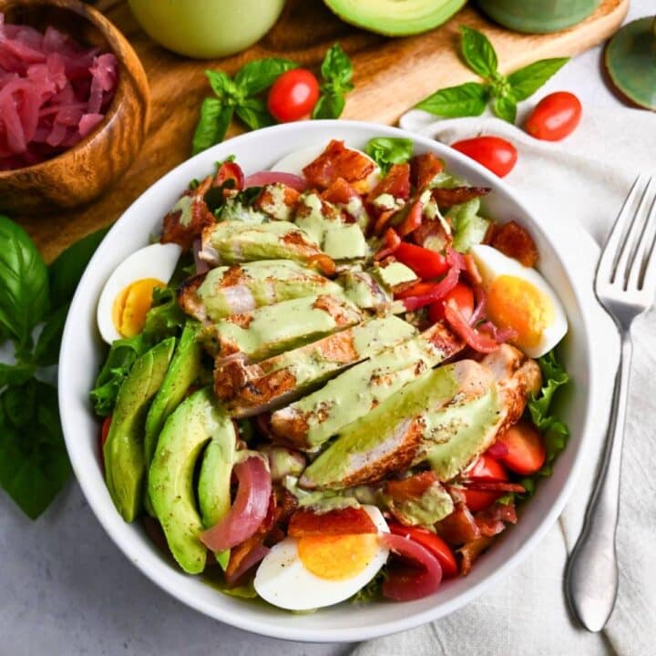 a green goddess chicken salad with a cutting board with avocado and dressing behind it